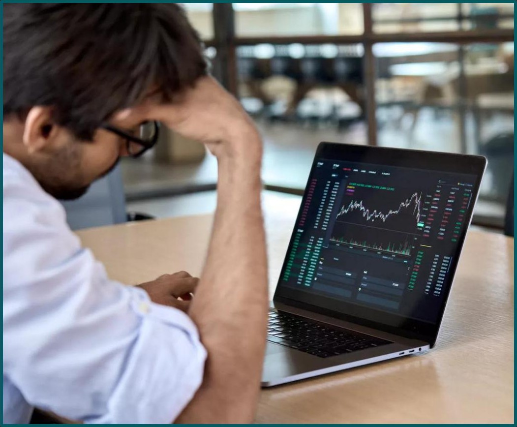 Frustrated retail trader looking at a losing position on a laptop trading terminal